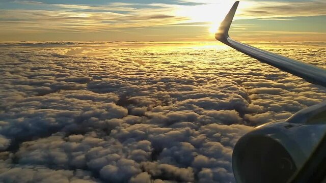 Sunrise from above the clouds with jet's wing and engine.