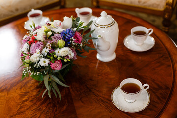 Сups of tea, teapot and bouquet of garden pink and white roses on a wooden table