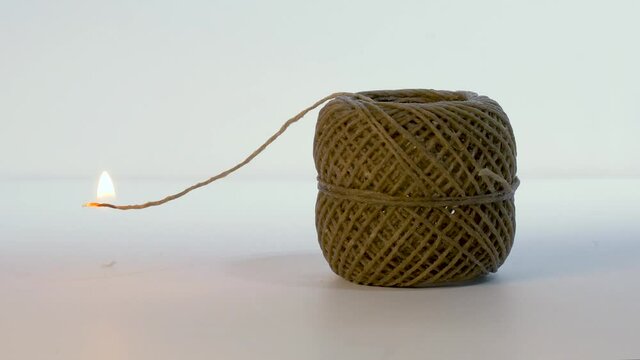 Ball of natural wax coated hemp wick.  Small ball of wound up hemp wick, lit from one end, flame slowly burning towards ball.  Concept video showing time running out, or material being wasted.