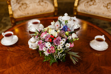 Four cups of tea, teapot and sugar bowl on wooden table. Bouquet of fresh garden pink and white flowers in the center of composition