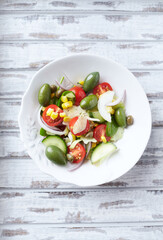 Mediterranean-style Salad with Green Olives, Cucumber, Cherry Tomatoes and Capers. Bright wooden background. Top view. 
