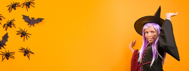 Enthusiastic little girl in a witch costume . Person posing on a yellow background in the studio. Copy space. High quality photo. Banner