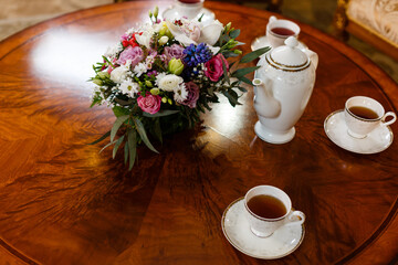 Сups of tea, teapot and bouquet of garden pink and white roses on a wooden table