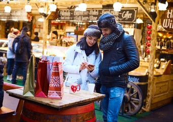 Young couple doing christmas shopping at christmas fair, using mobilephone.