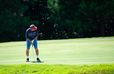 A man golfer putting a golf ball on a golf green with a pin at a golf course country club