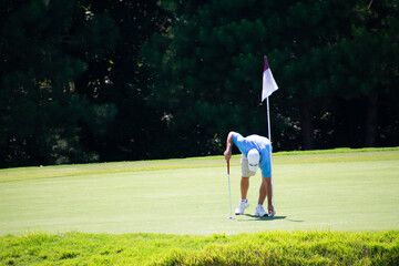 A male man golfer hitting a golf ball to the green with a pin with an iron wedge in the ruff rough at a golf course country club