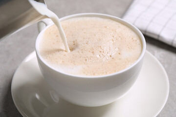 Pouring milk into cup of coffee on grey table, closeup