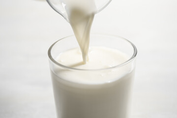 Pouring milk into glass on white table, closeup