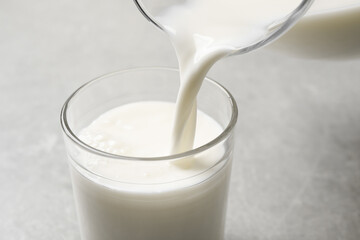 Pouring milk into glass on grey table, closeup