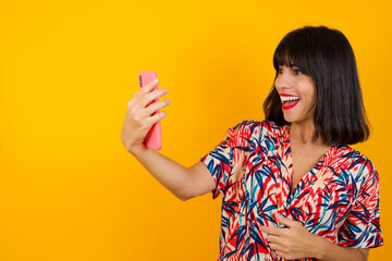 Portrait of a happy cheerful woman celebrating success while standing and looking at mobile phone isolated over bright background.