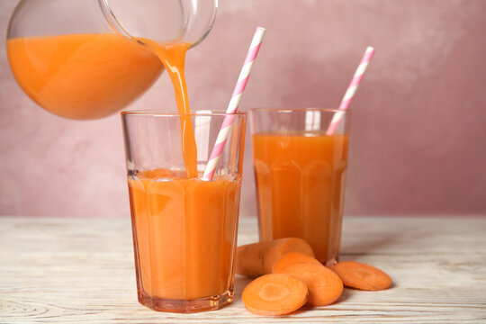 Pouring freshly made carrot juice into glass on wooden table