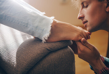 Handsome young man kissing woman's bare feet.
