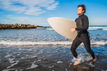 Surfer leaving the water with surfboard under his arm.