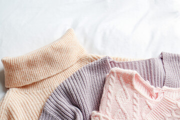 Obraz na płótnie Canvas Stylish knitted sweaters on white fabric, flat lay