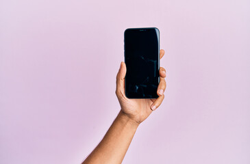 Hand of young hispanic man showing smartphone over isolated pink background.