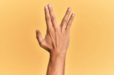 Arm and hand of caucasian man over yellow isolated background greeting doing vulcan salute, showing back of the hand and fingers, freak culture