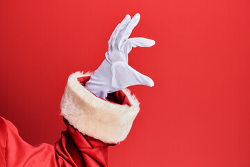 Hand of a man wearing santa claus costume and gloves over red background picking and taking invisible thing, holding object with fingers showing space