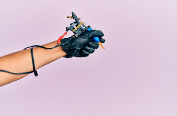 Obraz premium Hand of young hispanic man using tattoo machine over isolated pink background.