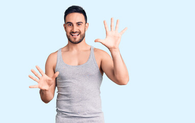 Young handsome man wearing swimwear and sleeveless t-shirt showing and pointing up with fingers number ten while smiling confident and happy.