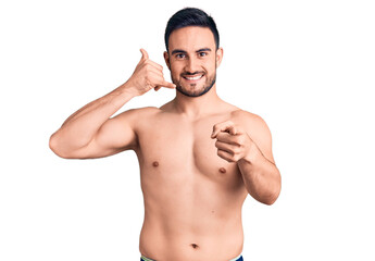 Fototapeta premium Young handsome man wearing swimwear smiling doing talking on the telephone gesture and pointing to you. call me.
