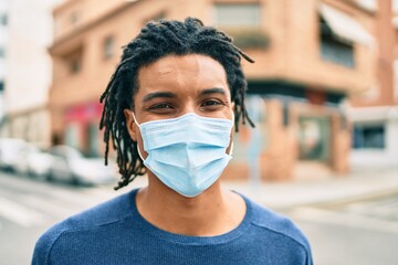 Young african american man wearing medical mask looking to the camera at street of city.