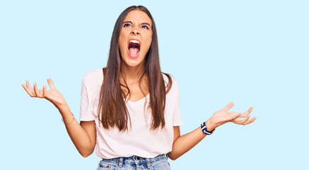 Fototapeta na wymiar Young hispanic woman wearing casual white tshirt crazy and mad shouting and yelling with aggressive expression and arms raised. frustration concept.