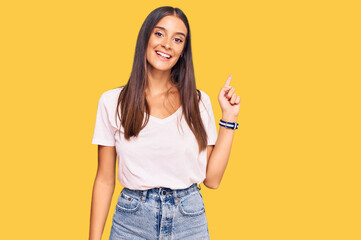 Young hispanic woman wearing casual white tshirt with a big smile on face, pointing with hand finger to the side looking at the camera.