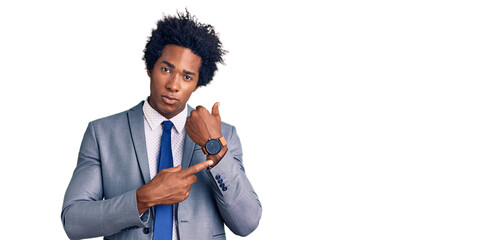 Handsome african american man with afro hair wearing business jacket in hurry pointing to watch...