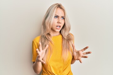 Beautiful caucasian blonde girl wearing casual tshirt crazy and mad shouting and yelling with aggressive expression and arms raised. frustration concept.