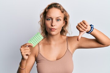 Beautiful caucasian woman holding birth control pills with angry face, negative sign showing...