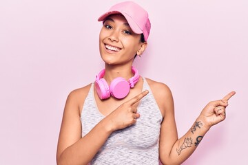 Young woman listening to music using headphones smiling and looking at the camera pointing with two hands and fingers to the side.