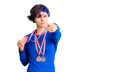 Beautiful young woman with short hair wearing winner medals pointing with finger to the camera and to you, confident gesture looking serious