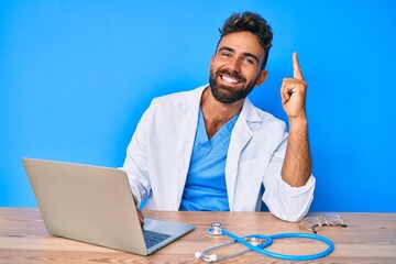 Young hispanic man wearing doctor uniform working at the clinic surprised with an idea or question pointing finger with happy face, number one