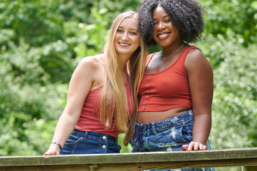 Two beautiful female friends pose for photo in park on summer day - nearly matching tank tops