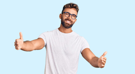 Young hispanic man wearing casual clothes and glasses looking at the camera smiling with open arms for hug. cheerful expression embracing happiness.