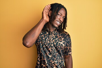 African american man with braids wearing leopard animal print shirt smiling with hand over ear listening an hearing to rumor or gossip. deafness concept.