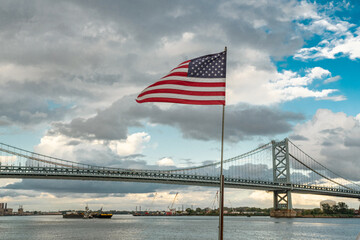 Fototapeta na wymiar Benjamin franklin bridge as seen from penn's landing in philadelphia flag
