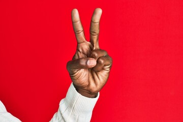 Arm and hand of african american black young man over red isolated background counting number 2 showing two fingers, gesturing victory and winner symbol