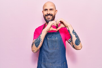 Young handsome man wearing apron smiling in love doing heart symbol shape with hands. romantic concept.