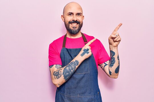 Young handsome man wearing apron smiling and looking at the camera pointing with two hands and fingers to the side.