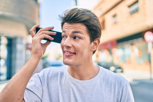 Young caucasian man smiling happy listening audio message using smartphone at the city.