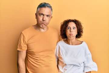 Beautiful middle age couple together wearing casual clothes puffing cheeks with funny face. mouth inflated with air, crazy expression.