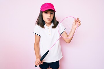Young little girl with bang holding badminton racket clueless and confused expression. doubt concept.