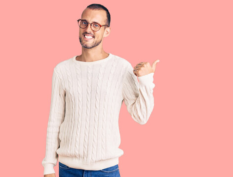 Young handsome man wearing casual clothes and glasses smiling with happy face looking and pointing to the side with thumb up.