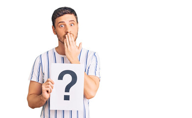 Handsome young man with bear holding question mark covering mouth with hand, shocked and afraid for...