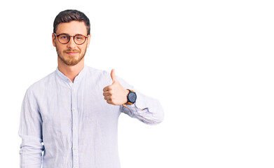 Handsome young man with bear wearing elegant business shirt and glasses doing happy thumbs up gesture with hand. approving expression looking at the camera showing success.