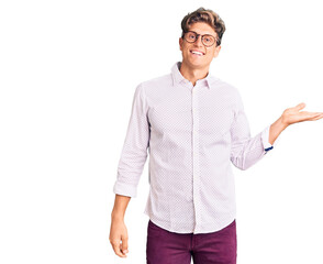 Fototapeta premium Young handsome man wearing business clothes and glasses smiling cheerful presenting and pointing with palm of hand looking at the camera.