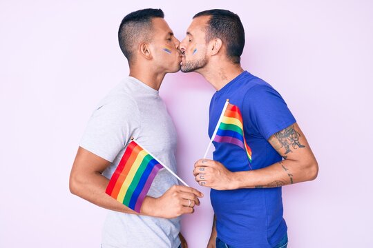 Young couple of gay men together in love holding homosexual pride colorful flag kissing with affection