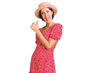 Young beautiful woman wearing summer hat doing happy thumbs up gesture with hand. approving expression looking at the camera showing success.