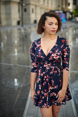 Beautiful biracial woman in floral print dress poses among fountains in city plaza